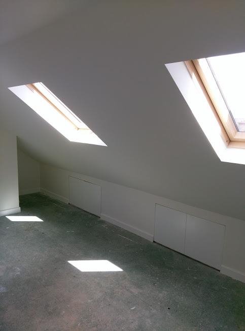 Poddasze po remoncie z dwoma oknami dachowymi i zabudowanymi schowkami w ścianie kolankowej, widoczne plamy światła na podłodze.