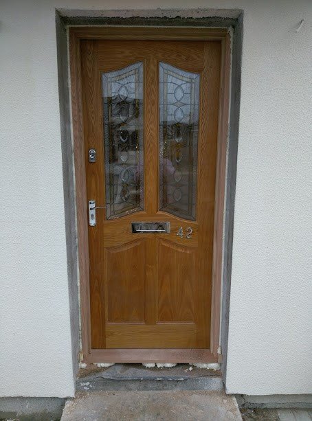 Nowa drewniana dębowa drzwi wejściowe z szybami i numerem 42, zamontowana w surowym otworze drzwiowym przed ostatecznym wykończeniem.