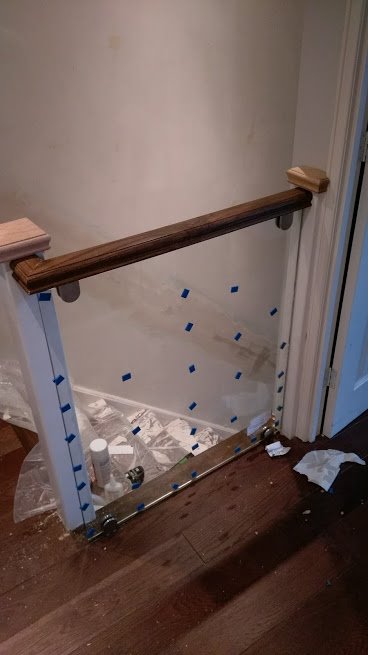 Szklana balustrada schodowa w trakcie montażu, zabezpieczona niebieską taśmą malarską, widoczne narzędzia i folia ochronna.