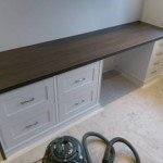 Szara zabudowa meblowa z ciemnym blatem w Romford, widoczne szuflady z metalowymi uchwytami i otwarta przestrzeń na nogi, na podłodze odkurzacz.