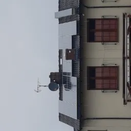 Panele słoneczne zamontowane na dachu domu jednorodzinnego z anteną satelitarną, widok z dołu na szarym tle nieba.