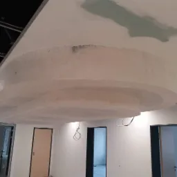 Niedokończona, wielopoziomowa konstrukcja sufitu podwieszanego z płyt kartonowo-gipsowych, widoczne szpachlowanie i łączenia, surowy stan wykończenia, wnętrze w trakcie modernizacji.