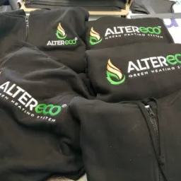 Stos czarnych bluz z zamkiem błyskawicznym i haftowanym logo Altereco Green Heating System, widoczne detale haftu i tekstury materiału