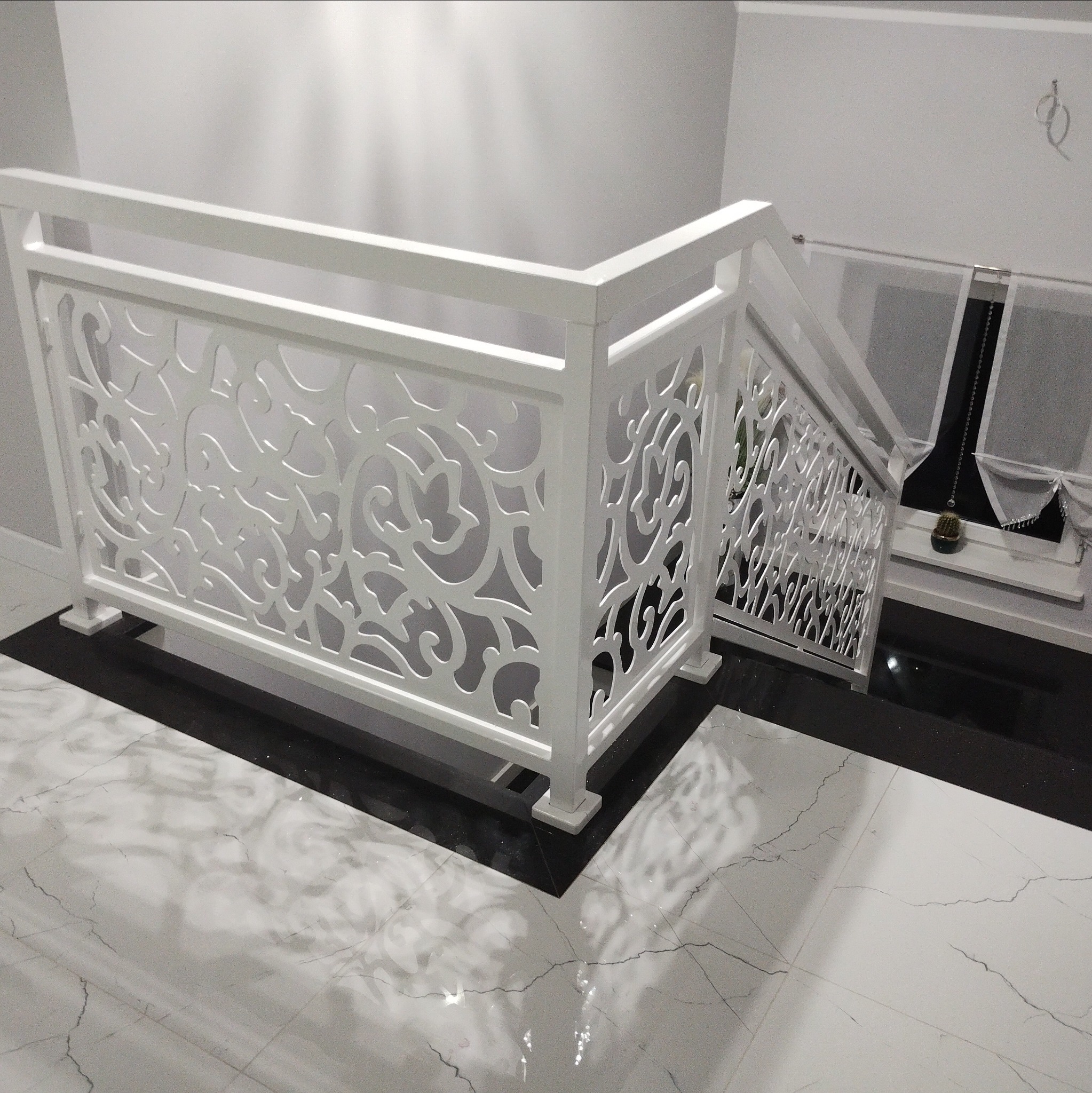 Biała, ażurowa balustrada schodowa z dekoracyjnym wzorem na marmurowej posadzce. Nowoczesny design, eleganckie wykończenie.