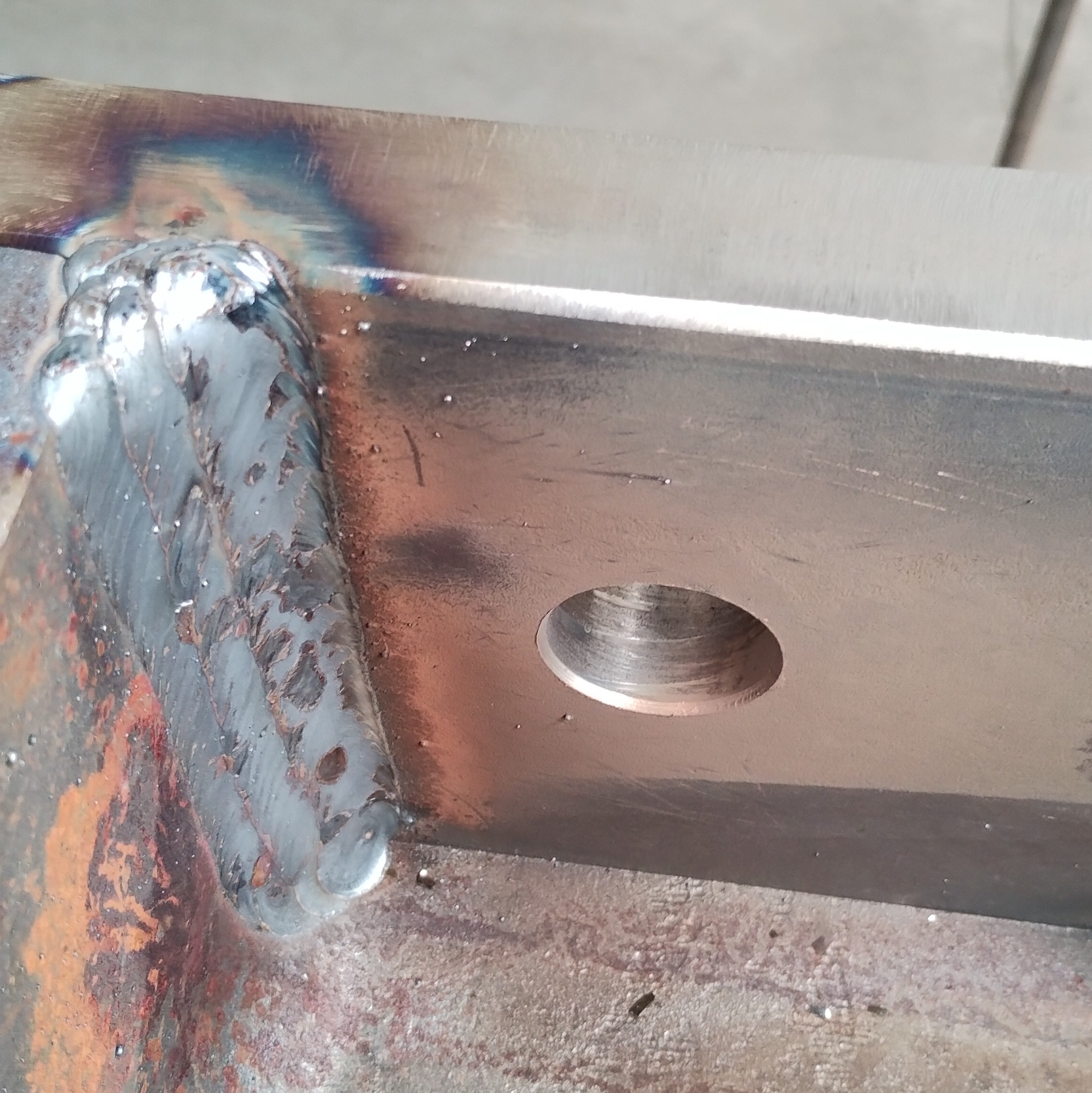 Spoina na metalowym elemencie z otworem, widoczne ślady po obróbce termicznej i spawaniu. Detal konstrukcyjny po procesie łączenia.