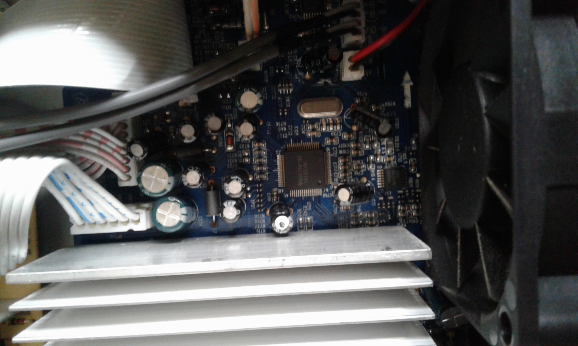 Płyta główna komputera z widocznym radiatorem, wentylatorem, kondensatorami i układami scalonymi, oświetlona sztucznym światłem.