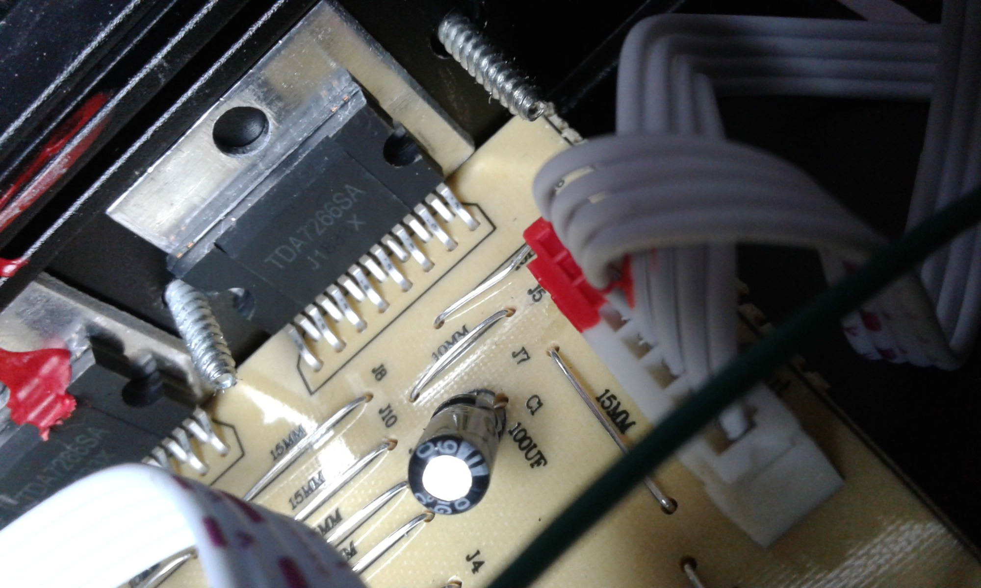 Zbliżenie na płytkę drukowaną z elementami elektronicznymi, w tym układ scalony TDA7266SA, kondensator i złącza kablowe, widoczne ślady lutowania.