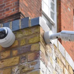 Dwie kamery monitoringu Hikvision zamontowane na rogu ceglanego budynku, jedna kopułkowa, druga cylindryczna, skierowane w różne strony.