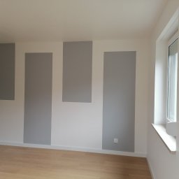 Wykończenie mieszkań - Pomalowane na biało ściany z szarymi, pionowymi pasami w nowym, pustym pokoju z drewnianą podłogą i oknem.