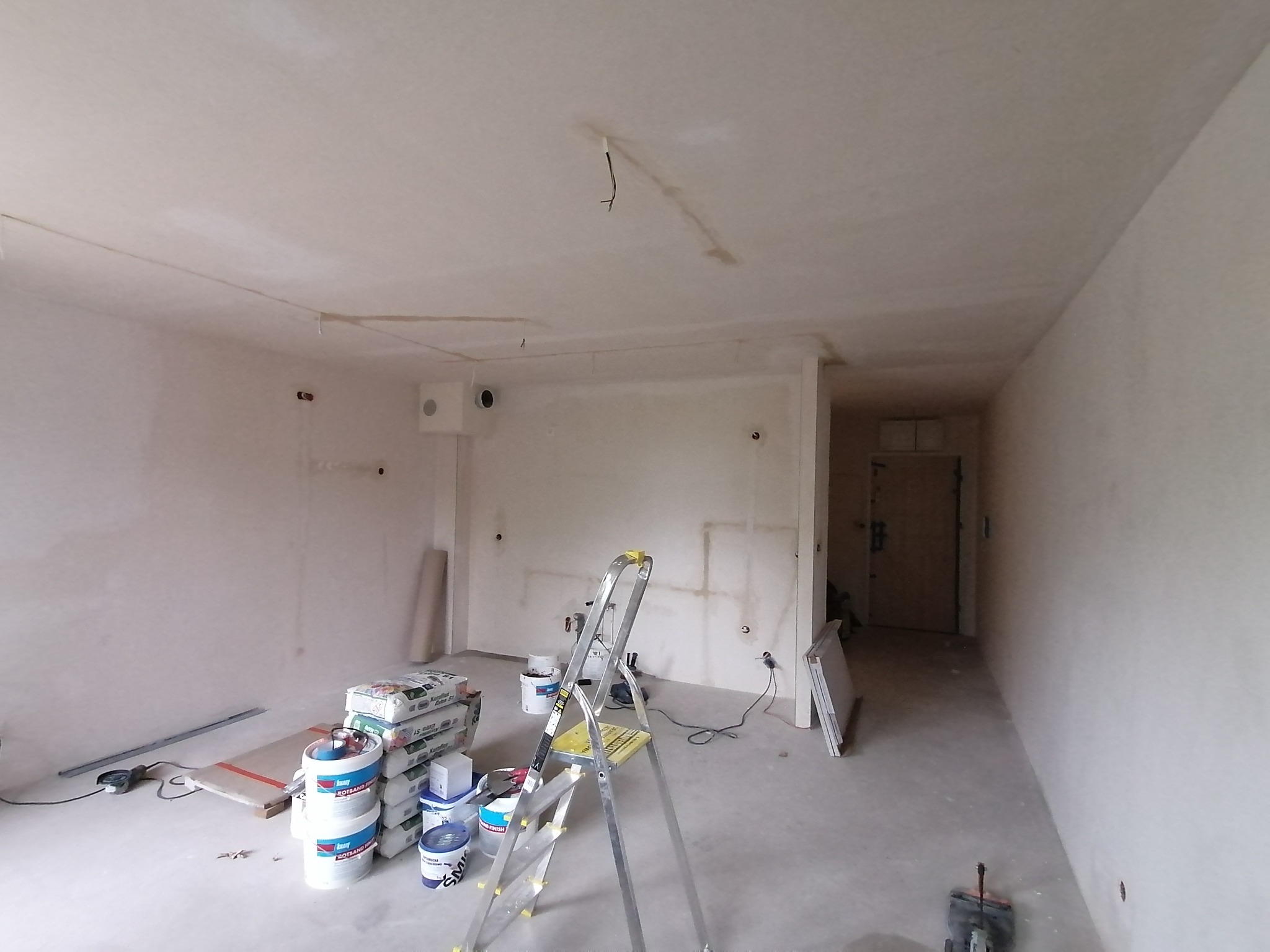Pokój w trakcie szpachlowania: widoczne worki z gładzią, wiadra z farbą, drabina, ściany pokryte szpachlą, przygotowane do malowania.