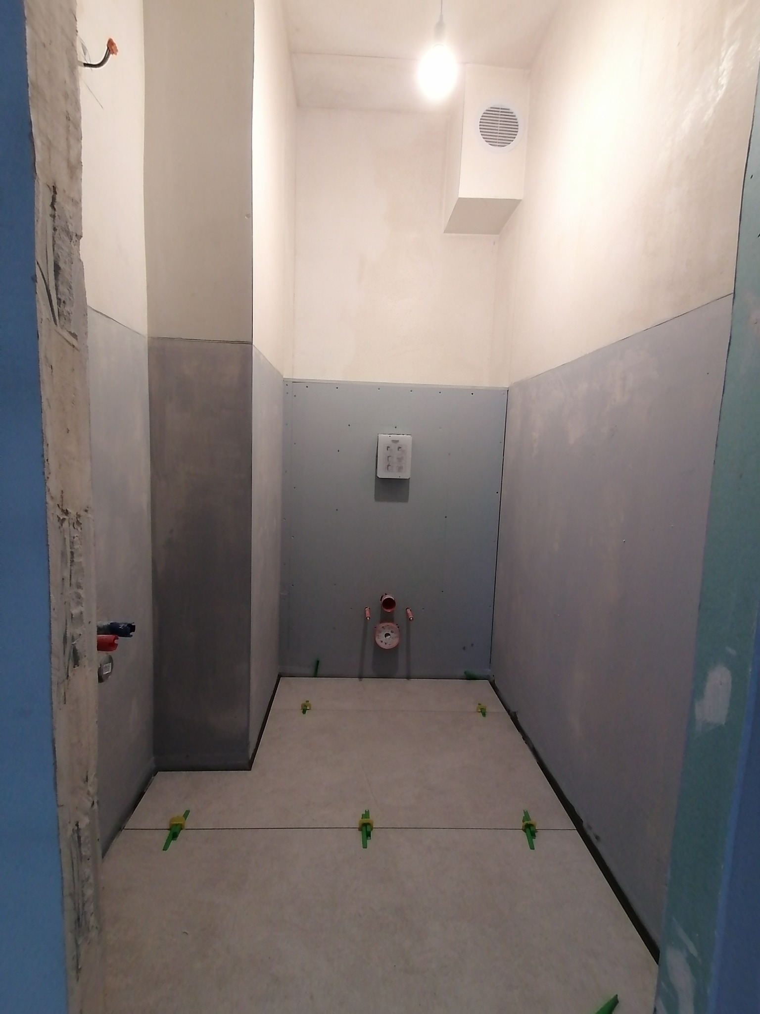 Łazienka w trakcie układania płytek podłogowych w Iwano-Frankowsku, widoczne krzyżyki dystansowe i wyprowadzenia instalacji wodnej.