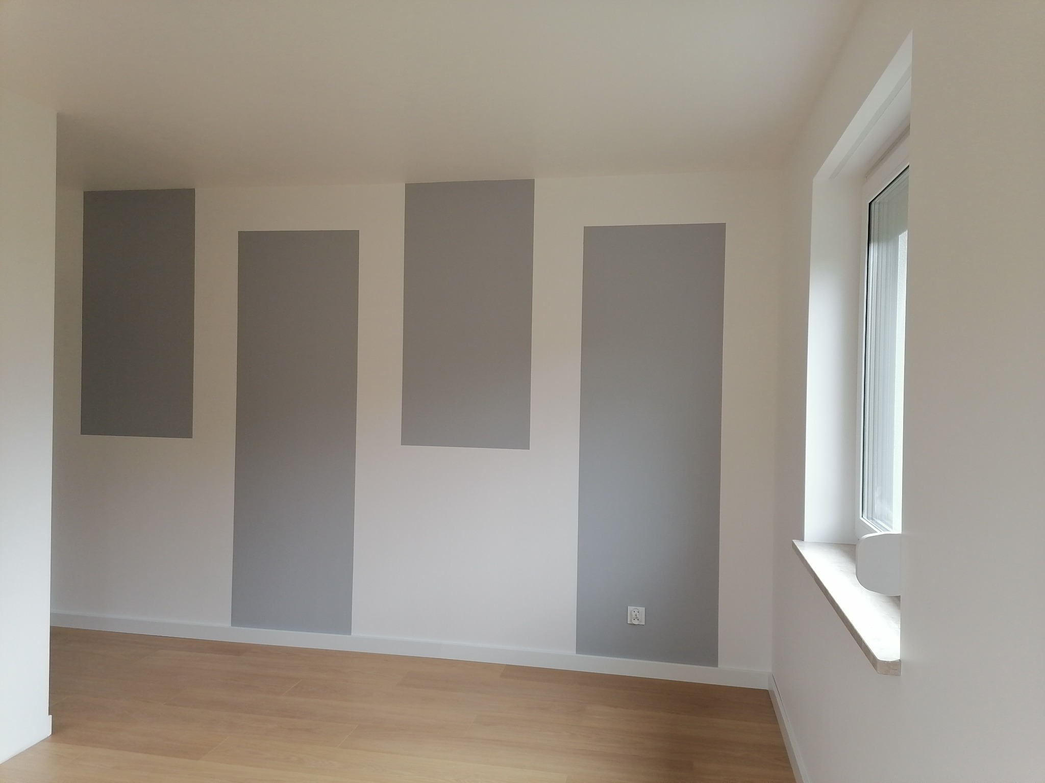 Pomalowane na biało ściany z szarymi, pionowymi pasami w nowym, pustym pokoju z drewnianą podłogą i oknem.