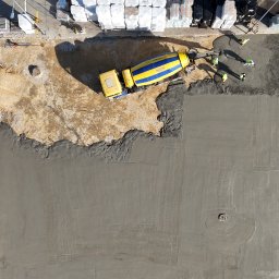 ZHUP MIRS - Widok z góry na wylewanie betonu z betoniarki, pracownicy wyrównują powierzchnię. Na placu budowy składowane materiały budowlane.