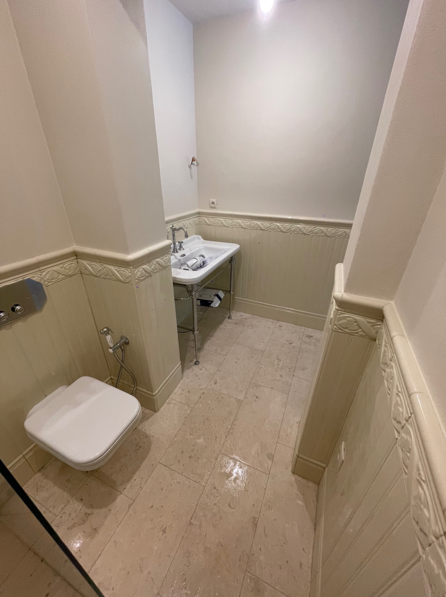 Klasyczna łazienka z beżowymi płytkami, białą ceramiką i dekoracyjnymi panelami ściennymi z subtelnym wzorem.