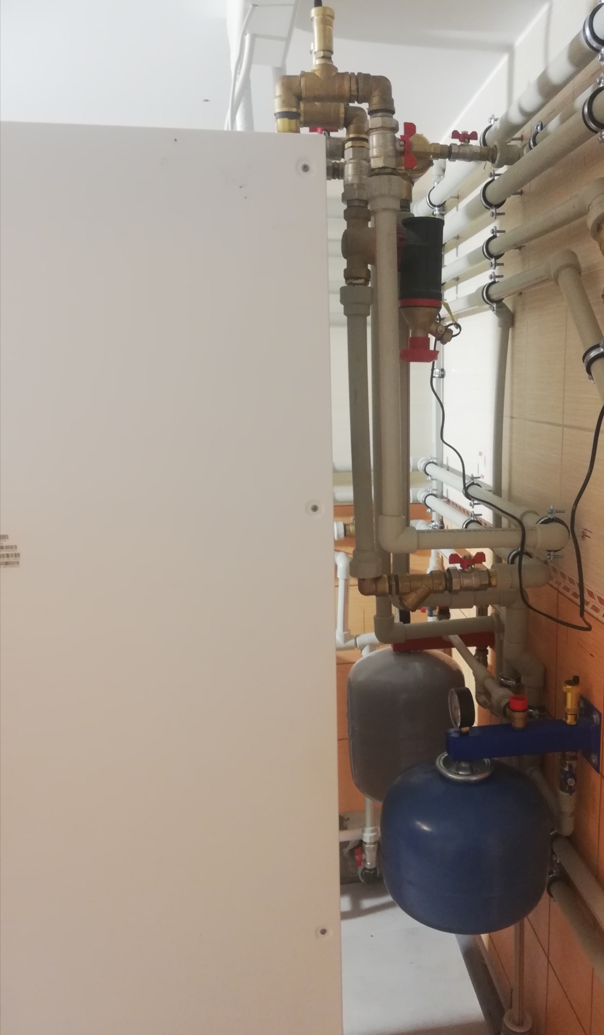 Instalacja z licznymi rurami, zaworami i zbiornikami w kotłowni w Warszawie, prawdopodobnie część systemu grzewczego.