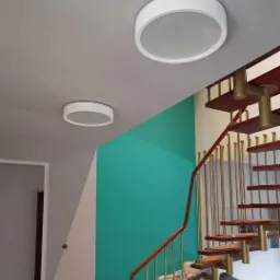 Nowoczesne, okrągłe lampy sufitowe LED w przedpokoju z turkusową ścianą i drewnianymi schodami z metalowymi balustradami.