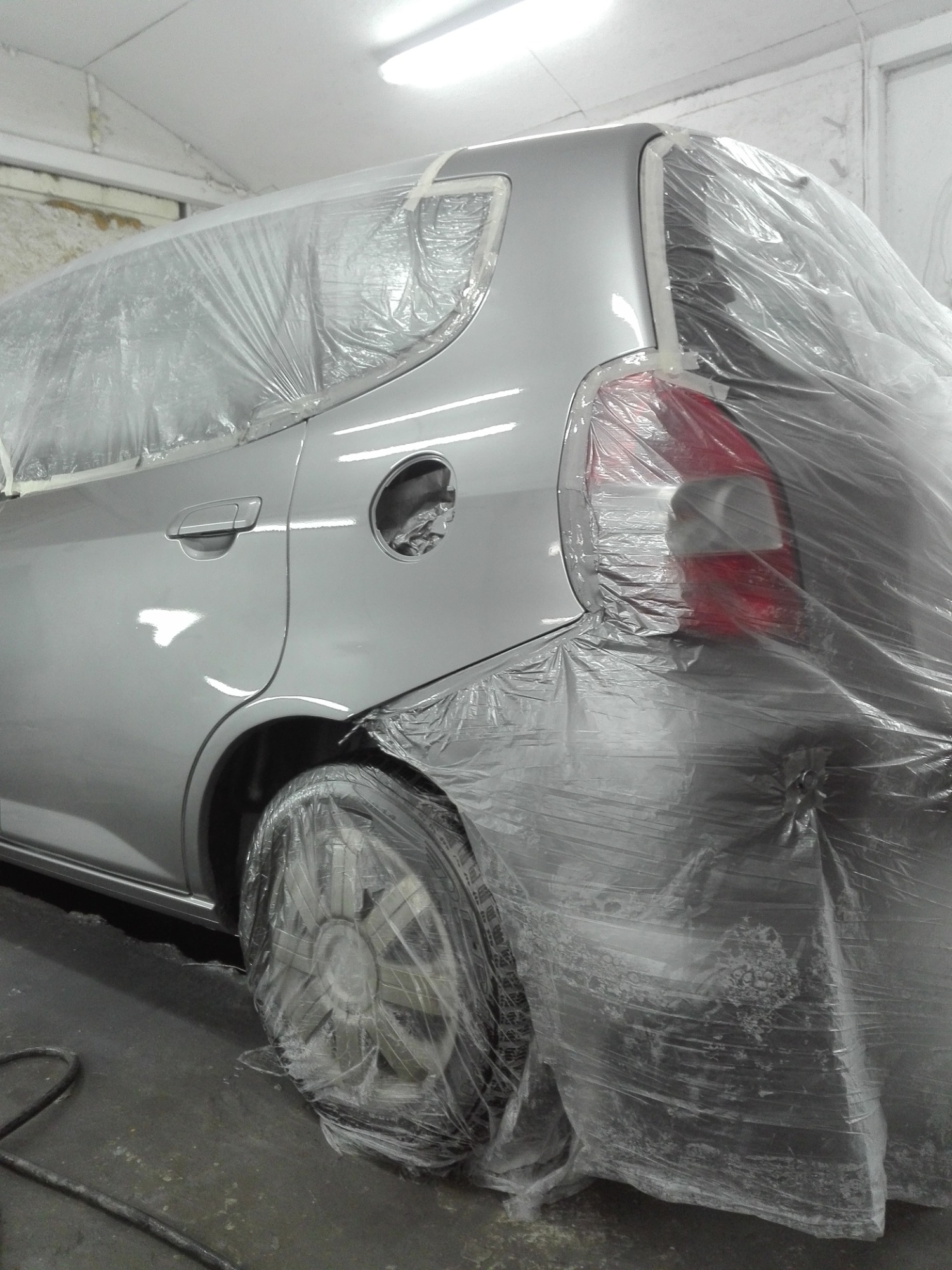 Samochód osobowy oklejony folią ochronną przed lakierowaniem, widoczne taśmy maskujące i zakryte koło, przygotowany do naprawy blacharsko-lakierniczej.