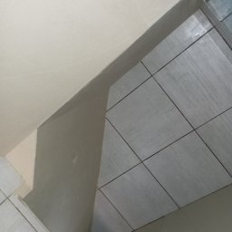 Tynki maszynowe - Szare płytki podłogowe ułożone w rogu pomieszczenia w Tarnogórze, widok z góry, świeżo po fugowaniu, z widocznymi fragmentami ścian.