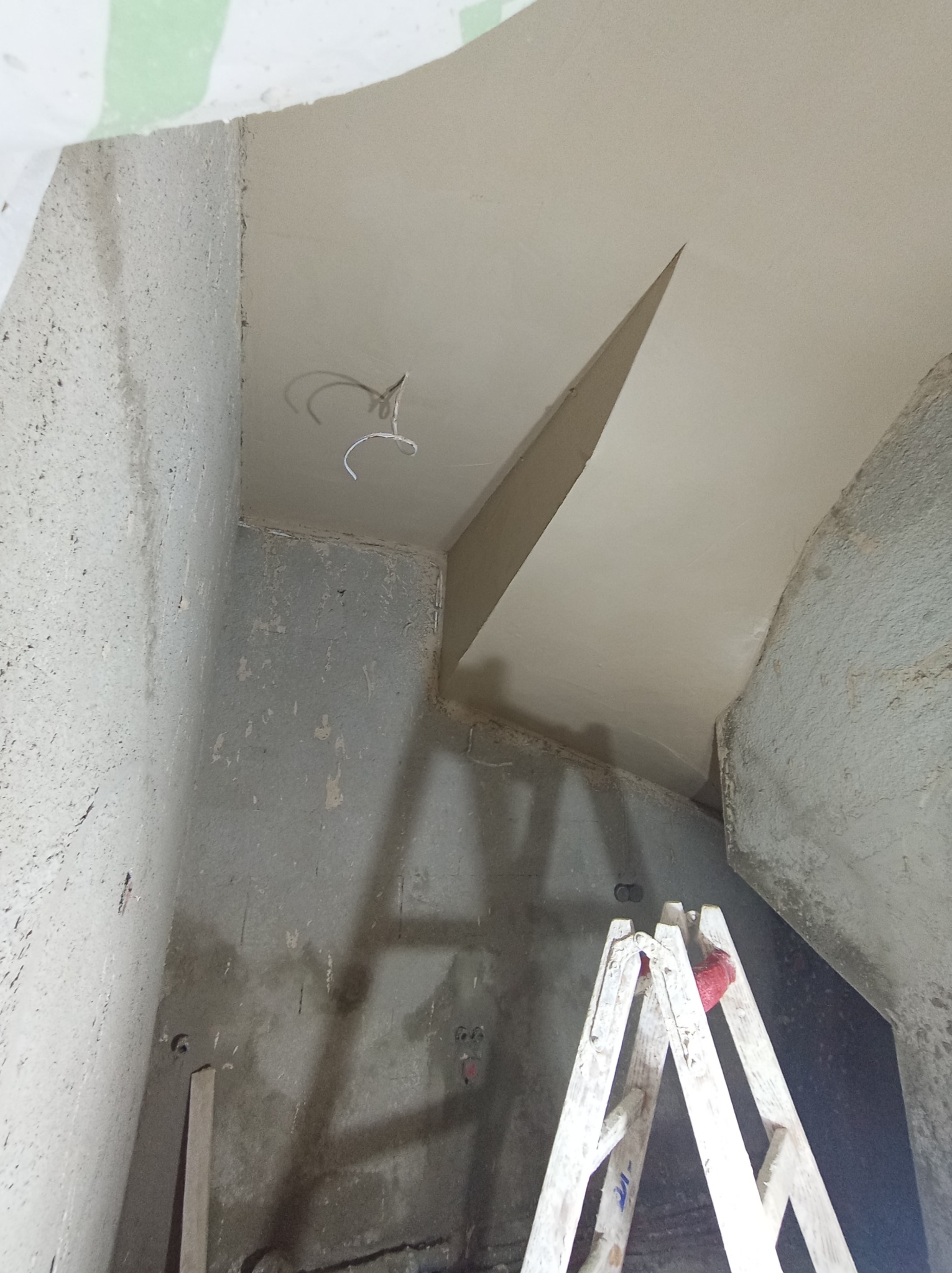 Wnętrze w trakcie prac wykończeniowych: surowe ściany, świeżo położone gładzie na suficie z wystającymi przewodami elektrycznymi, drabina malarska w rogu pomieszczenia.