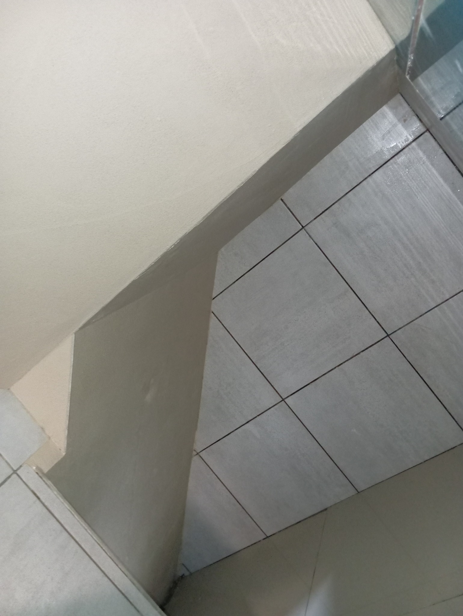 Szare płytki podłogowe ułożone w rogu pomieszczenia w Tarnogórze, widok z góry, świeżo po fugowaniu, z widocznymi fragmentami ścian.