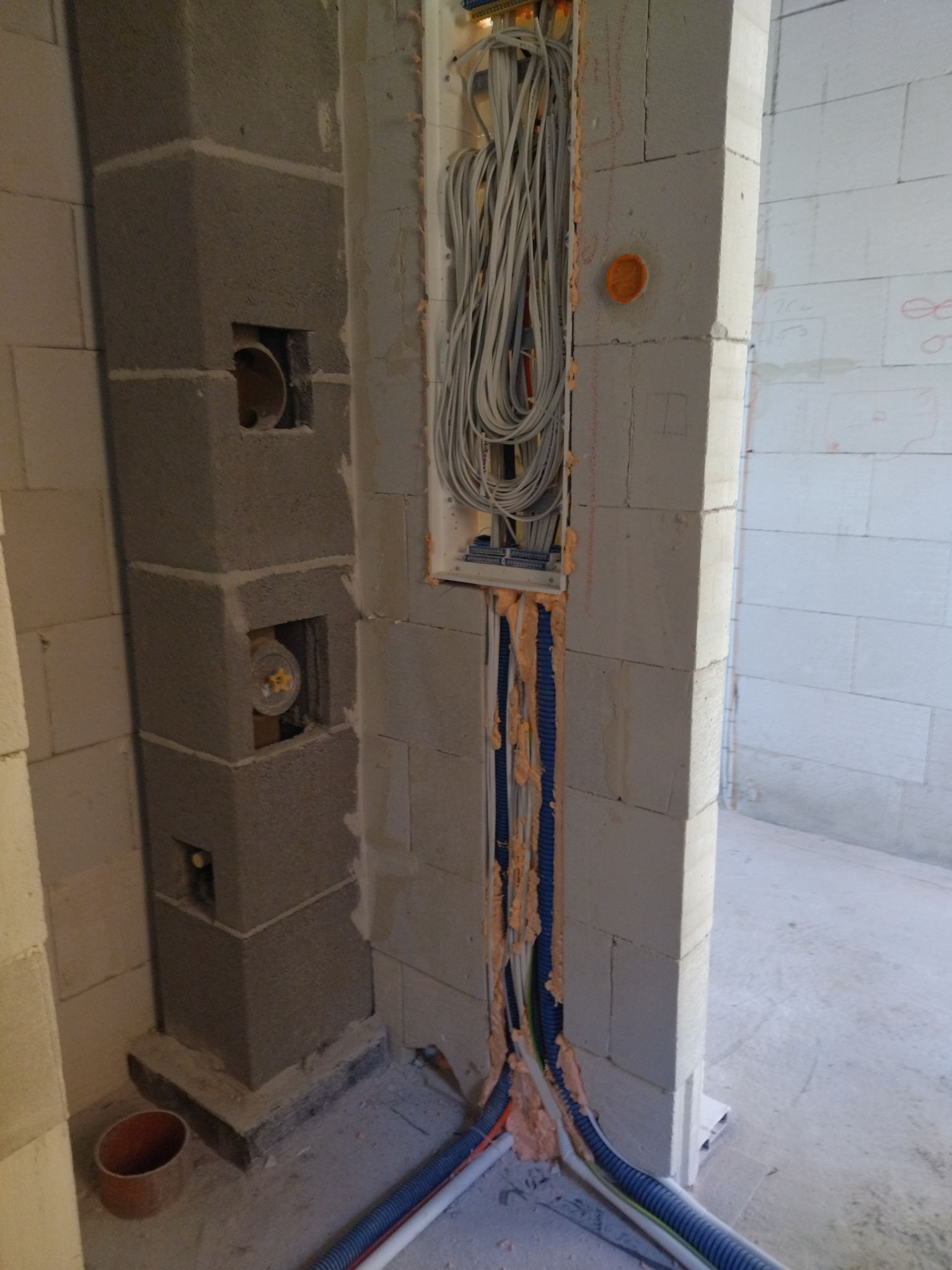 Wnęka w ścianie z instalacją elektryczną w trakcie montażu. Widoczne przewody, peszle i puszki instalacyjne. Ściana z betonu komórkowego.