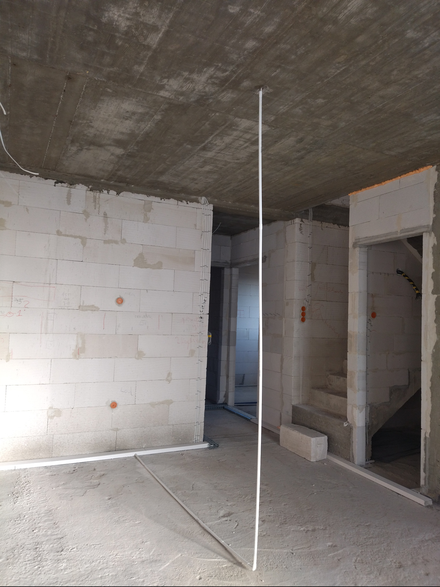 Surowy stan wnętrza: ściany z betonu komórkowego z widocznymi puszkami instalacyjnymi, przewody w listwach podłogowych i pionowy peszel pod sufitem.