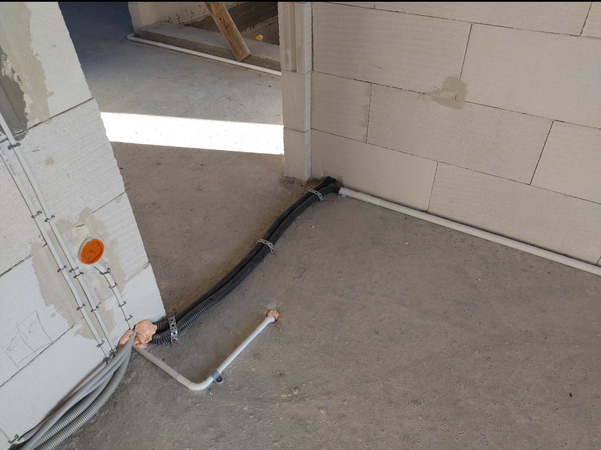 Wewnętrzna instalacja elektryczna w budynku w trakcie budowy. Kable w peszlach przymocowane do ściany i podłogi. Widoczne puszki instalacyjne.