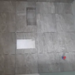 Ściana w trakcie układania płytek imitujących marmur w Środzie Śląskiej, z widocznym otworem na półkę i krzyżykami dystansowymi.