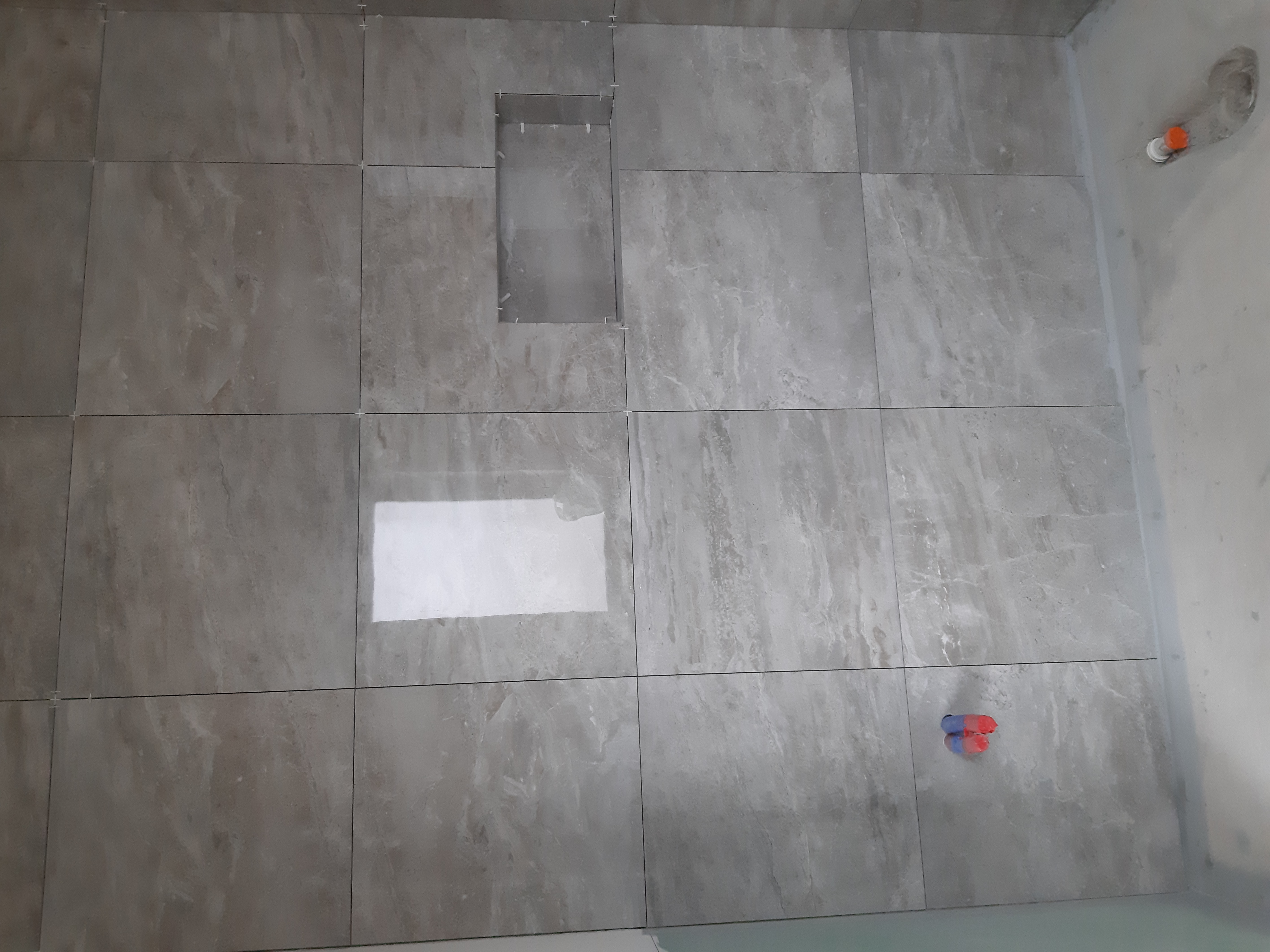 Ściana w trakcie układania płytek imitujących marmur w Środzie Śląskiej, z widocznym otworem na półkę i krzyżykami dystansowymi.