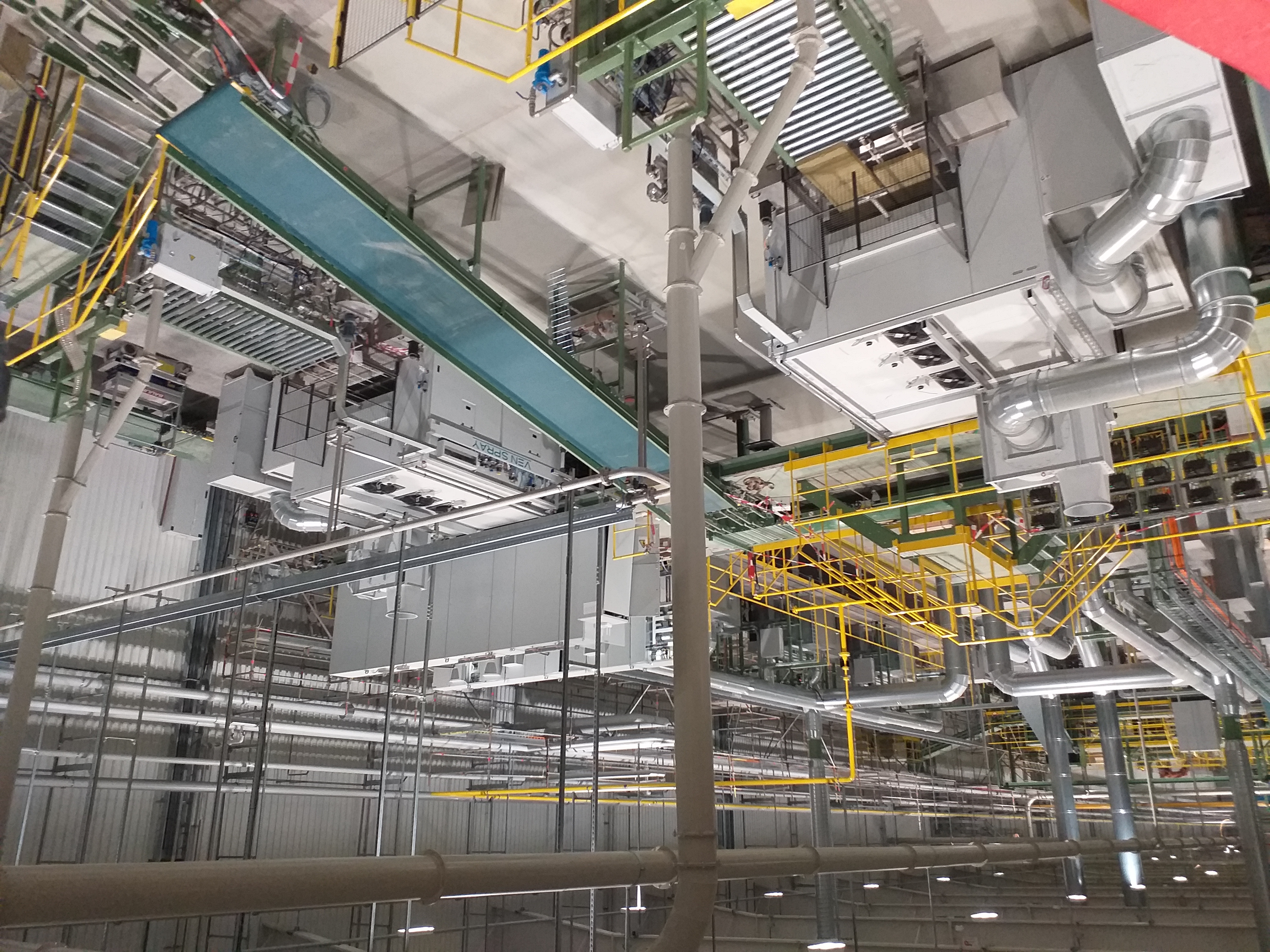 Kompleksowa instalacja przemysłowa z rurami, podestami i systemami wentylacyjnymi, widok z dołu, oświetlenie przemysłowe.