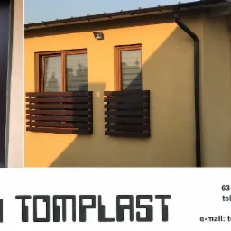 Nowoczesne drzwi wejściowe w kolorze ciemnego brązu z ozdobnym srebrnym paskiem, zamontowane w domu o żółtej elewacji z oknami z brązowymi ramami i roletami.