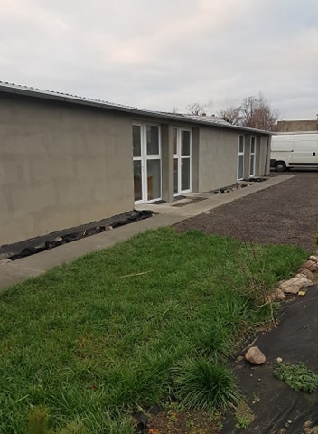 Budynek po montażu białych okien w Koźminie Wielkopolskim, widok z zewnątrz na szary, surowy tynk i zielony trawnik.