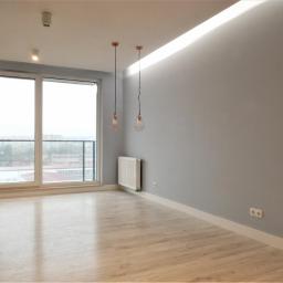 Bałabuch - Pomalowane na szaro wnętrze pokoju z panelami podłogowymi, białymi listwami przypodłogowymi, grzejnikiem, dwoma lampami wiszącymi w miedzianych kloszach i dużym oknem balkonowym.