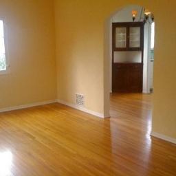 Bałabuch - Pomalowane na jasnożółto puste wnętrze z parkietem, widok na sąsiedni pokój przez łukowate przejście, w tle ciemne meble.