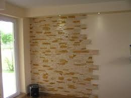 Fragment ściany w pokoju z dekoracyjnym wykończeniem z płytek imitujących kamień w odcieniach beżu i brązu, ułożonych częściowo na ścianie, sąsiadujących z gładką, pomalowaną powierzchnią. W rogu...