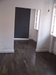 Pomalowane na biało ściany i ciemna ściana akcentowa w pokoju z parkietem, widok na sąsiednie pomieszczenie przez otwarte drzwi, minimalizm, widoczne listwy przypodłogowe.