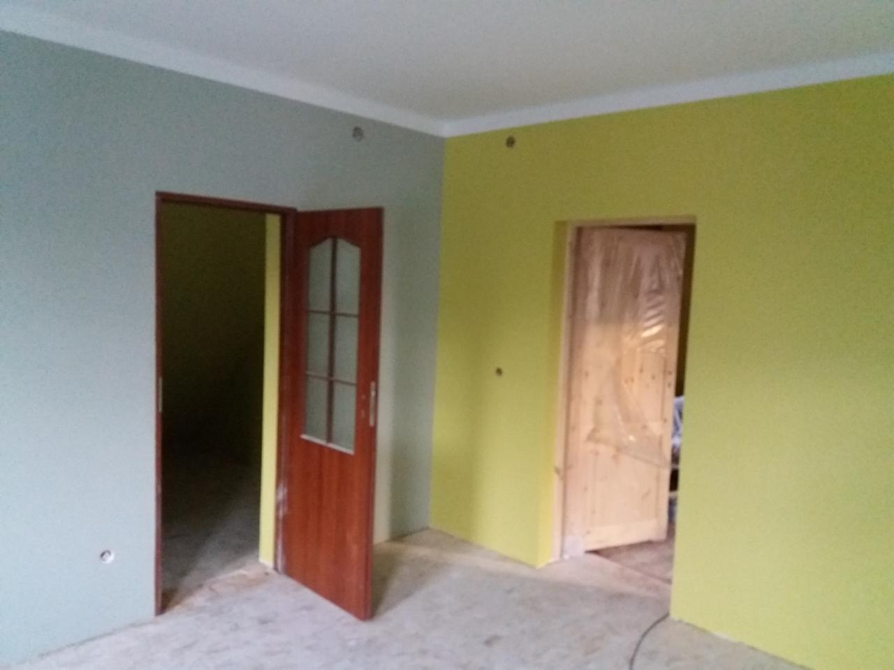 Pokój w trakcie malowania, ściany pomalowane na dwa kolory: szary i jasnożółty, widoczne dwoje drzwi, jedne drewniane z szybkami, drugie zabezpieczone folią malarską.