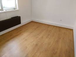 Pusty pokój po ułożeniu paneli podłogowych w odcieniach brązu; widoczna listwa przypodłogowa i grzejnik pod oknem.