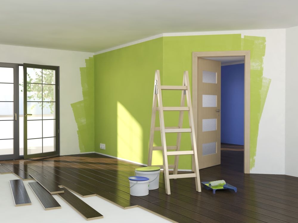 Wnętrze w trakcie remontu: częściowo pomalowana na zielono ściana, drewniane panele podłogowe w trakcie układania, drabina oparta o ścianę, dwa wiadra z farbą i wałek malarski