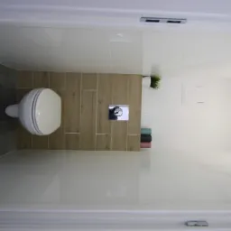 Nowoczesna, minimalistyczna toaleta podwieszana z szarą i drewnopodobną okładziną ścienną, widok z góry z elementami dekoracyjnymi w postaci rośliny doniczkowej i ręczników.