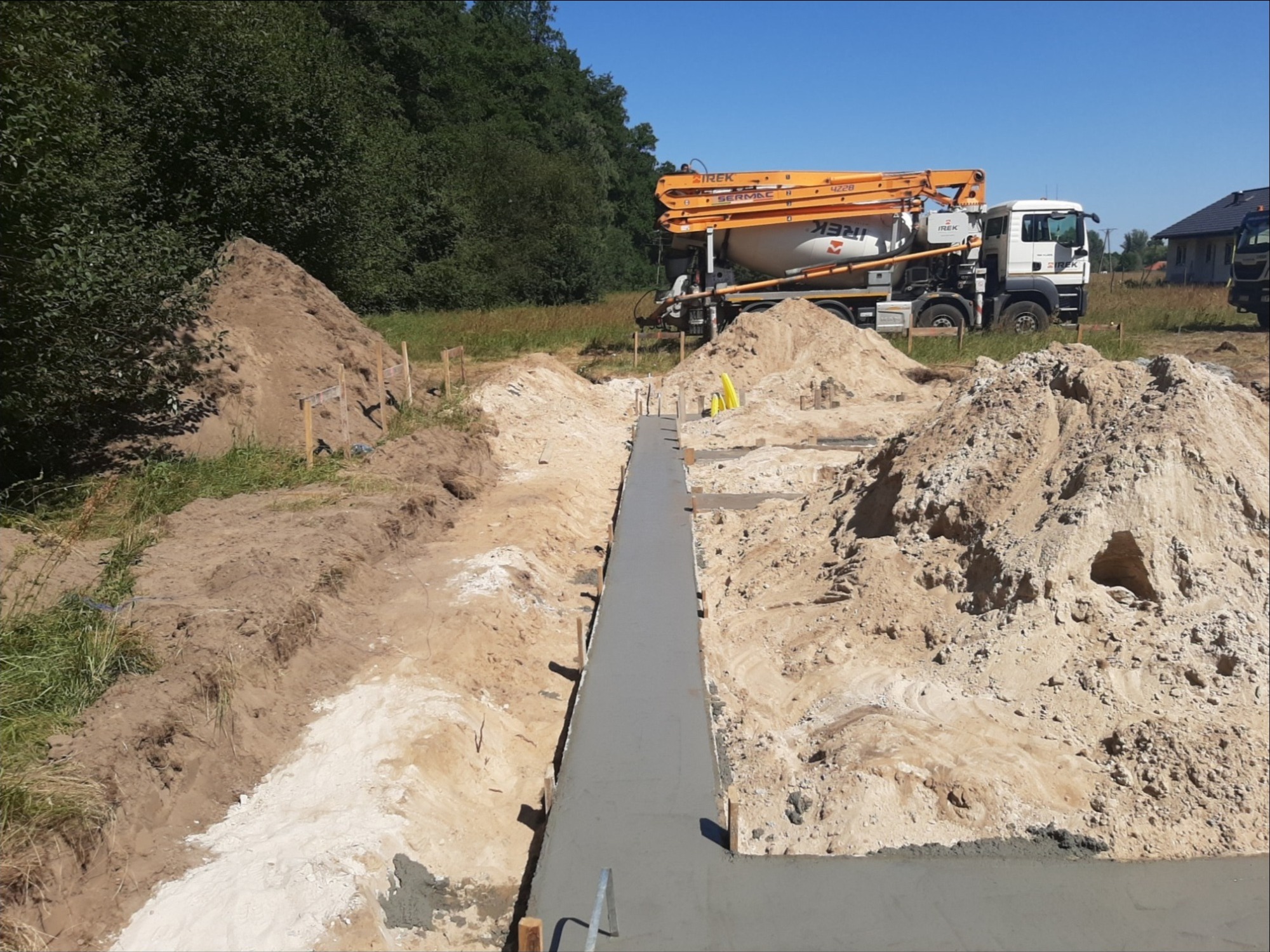 Wylany betonowy fundament w wykopie na budowie, z widocznym samochodem z pompą do betonu w tle.