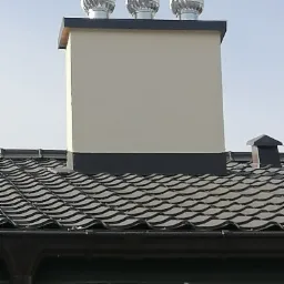 Komin wentylacyjny z trzema turbinami wiatrowymi na dachu z dachówki ceramicznej w odcieniach szarości.