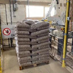 Paleta z workami pelletu w przezroczystych opakowaniach, obok robota przemysłowego ABB w hali produkcyjnej.