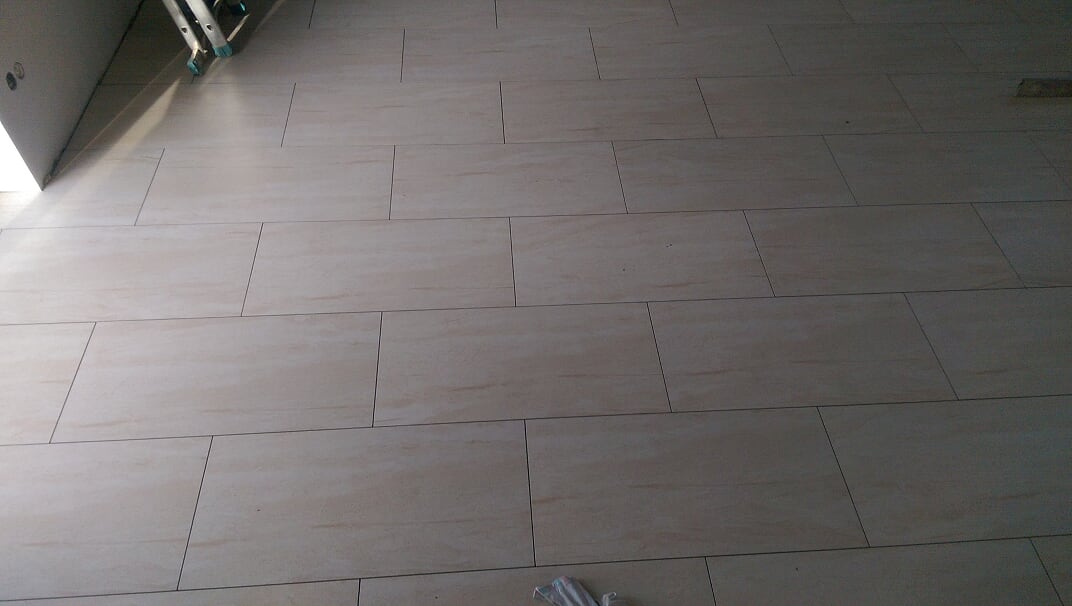 Ułożona podłoga z beżowych płytek imitujących kamień, widoczna drabina malarska oparta o ścianę.