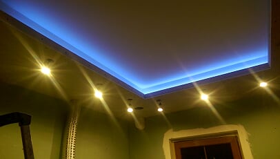 Podwieszany sufit z oświetleniem LED w kolorze niebieskim i punktowymi lampami halogenowymi, widoczna instalacja wentylacyjna i fragment drabiny.