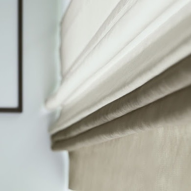 Beżowa, podciągana roleta rzymska z delikatnej tkaniny, widoczna z bliska, z fragmentem ramy obrazu w tle.