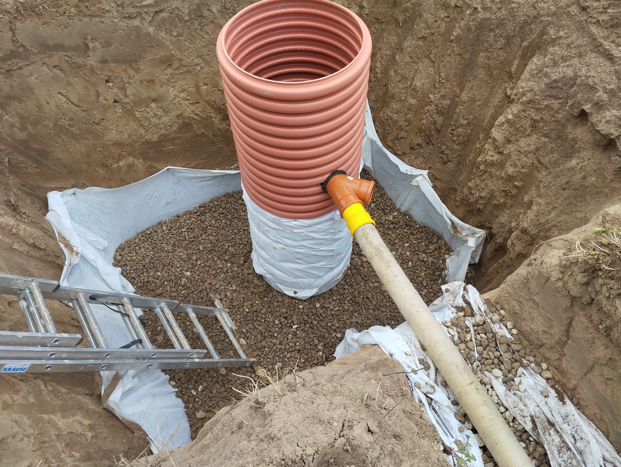 Montaż zbiornika z rurą w wykopie, obsypanego żwirem i zabezpieczonego geowłókniną. Widoczna drabina Krause.