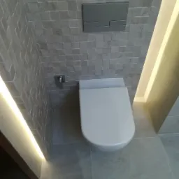 Podwieszana toaleta w łazience wykończonej płytkami w odcieniach szarości, z podświetleniem LED wzdłuż krawędzi ściany.