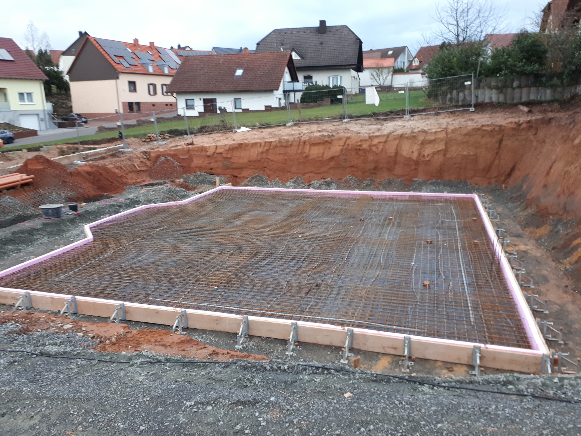 Przygotowanie fundamentów pod budynek: wykop, siatka zbrojeniowa, obrzeża z izolacją różową i szalunkiem drewnianym, grunt wokół wykopu.