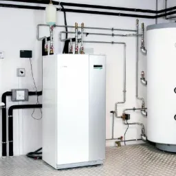 Biała kotłownia z piecem centralnego ogrzewania, zasobnikiem ciepłej wody, rurami i umywalką na tle białych ścian i metalowej podłogi.